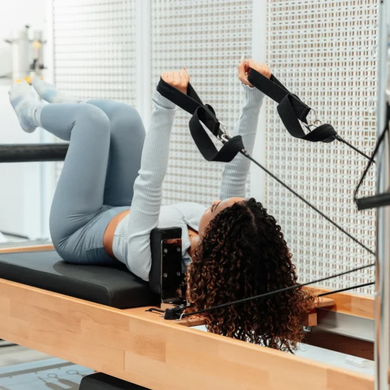 Woman performing Pilates exercises on a reformer machine, focusing on core strength.